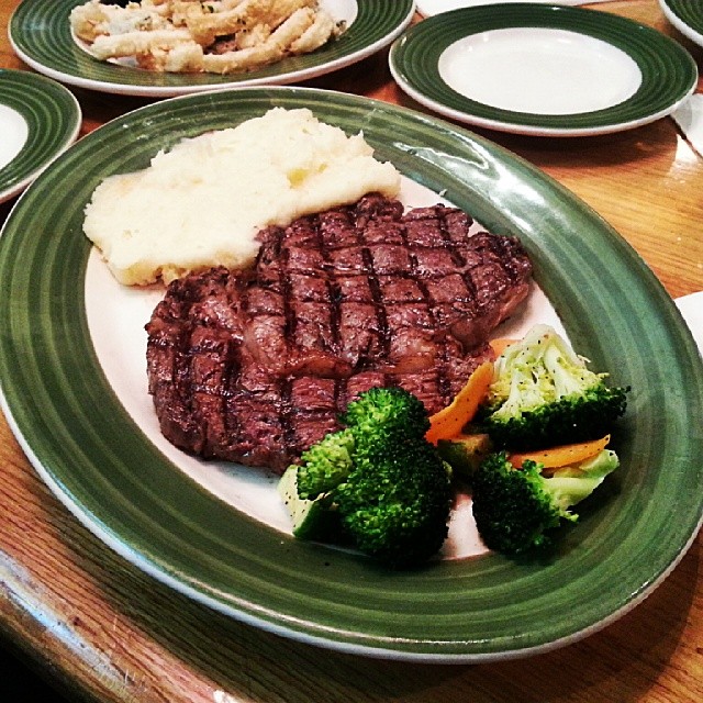 a large steak and broccoli on a green plate with four other plates of food