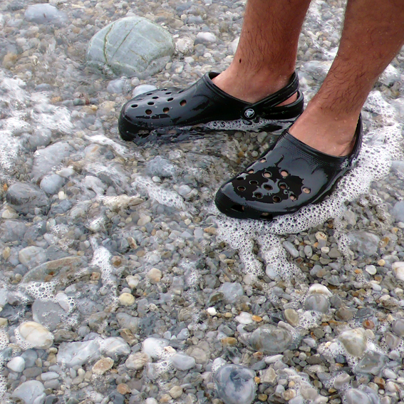 a man wearing a black flip flops stands on a rocky surface