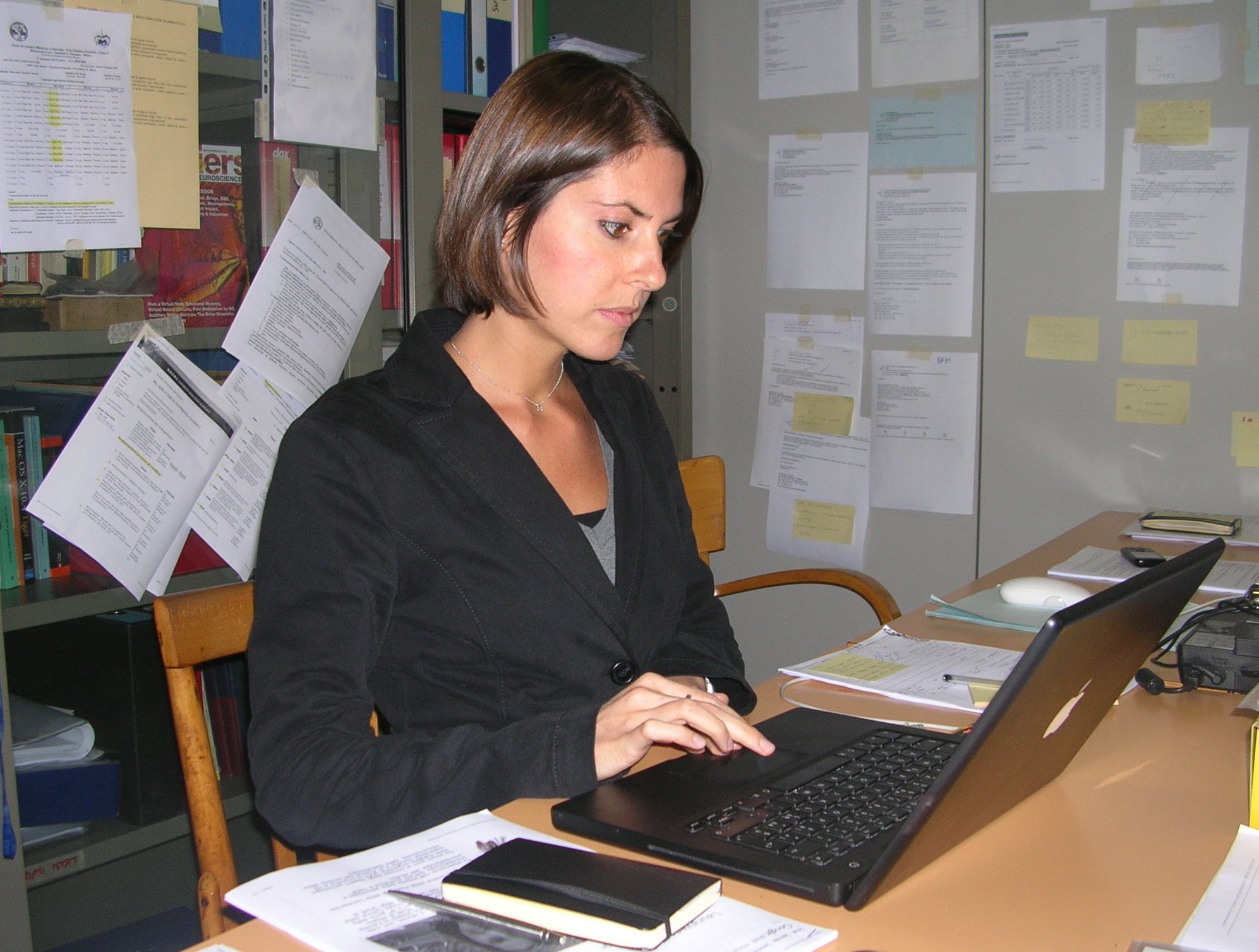 a woman is at her desk with a laptop and papers on the wall