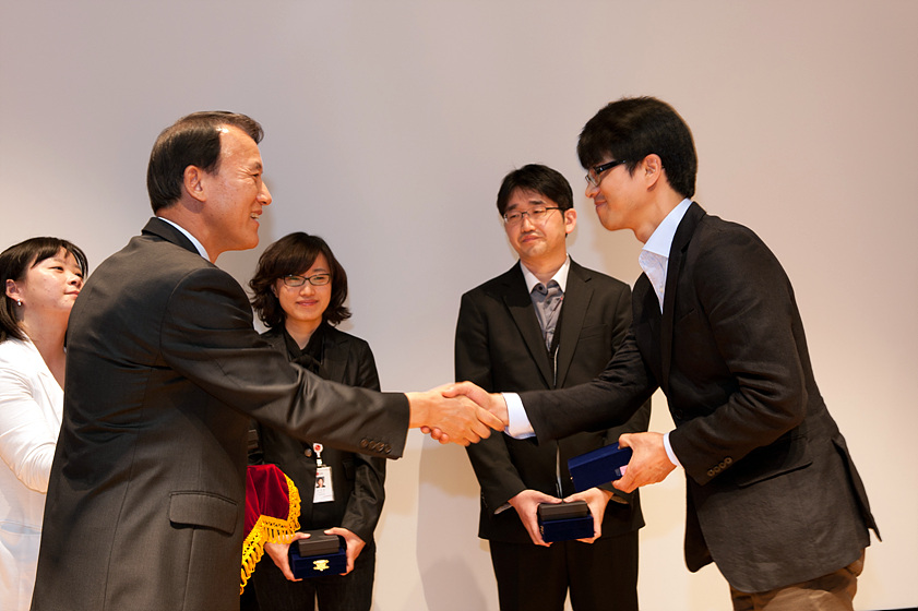 two men shake hands and smile in front of three other people