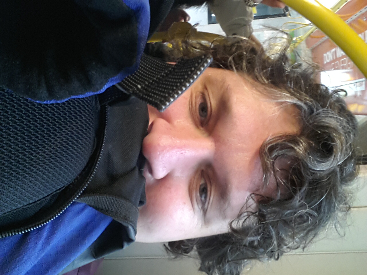 a man is sitting on a bus with curly hair and a backpack