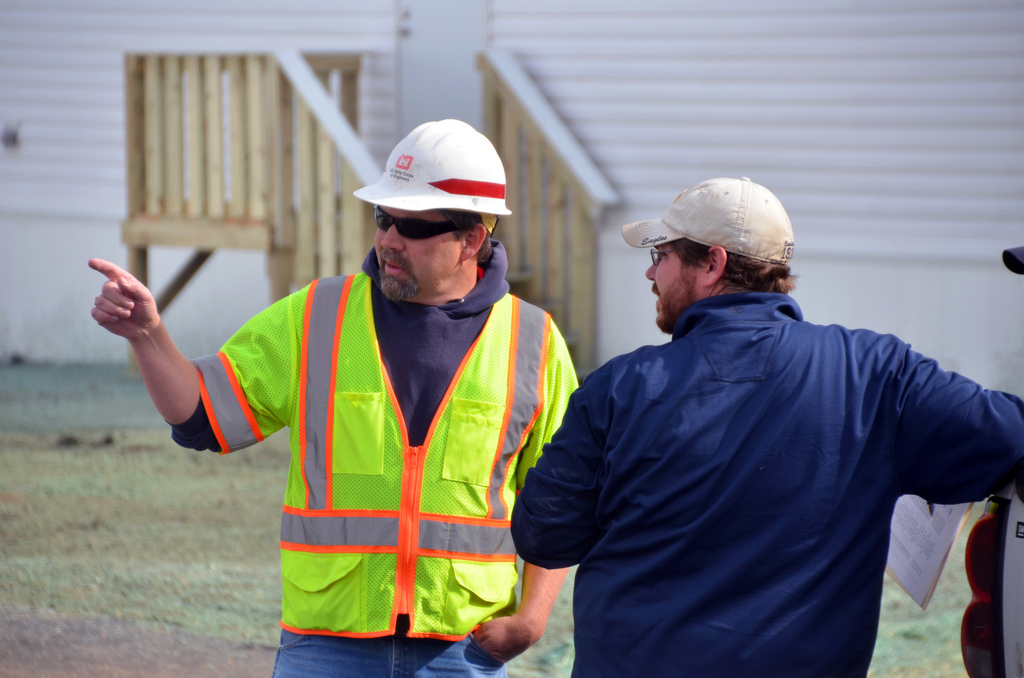 two men in safety vests and hard hats pointing at soing