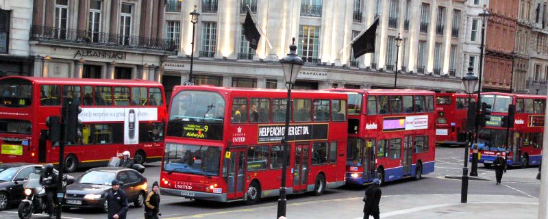 multiple red double decker buses are on the road