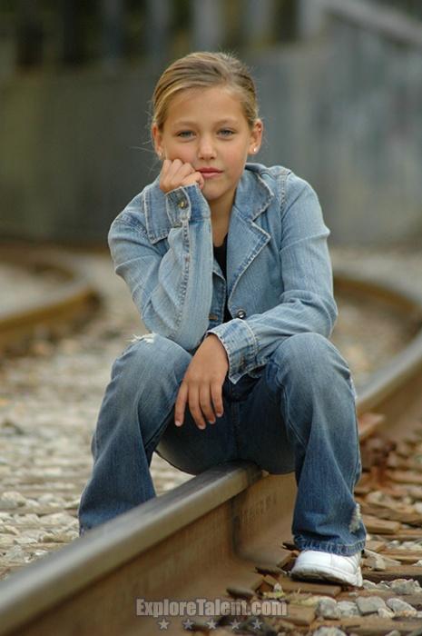 a girl sitting on train tracks with a hand in her mouth