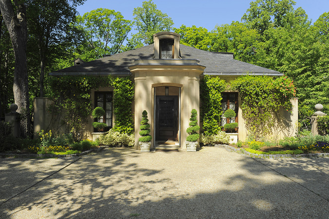 the entrance to a house sitting in front of a tree filled driveway