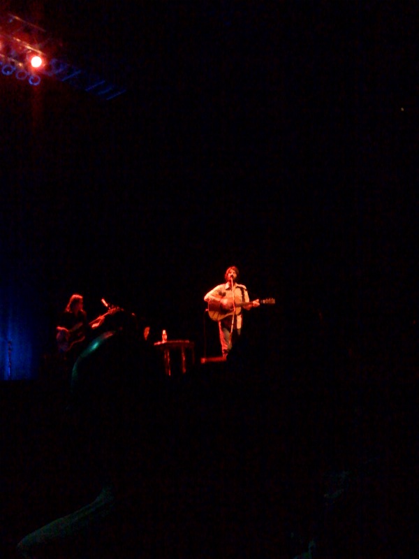 a guy on stage with a guitar next to another person