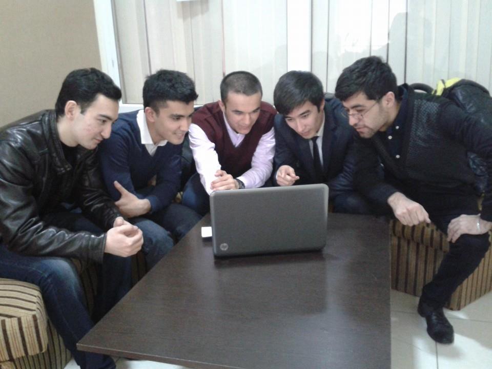group of people sitting around a computer with one pointing at the screen