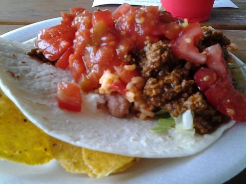 a taco covered with meat and sauce on top of corn tortilla