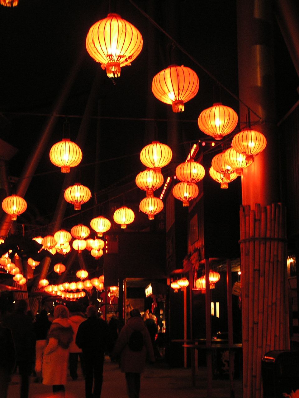 people walking down an alley with lanterns lit up at night