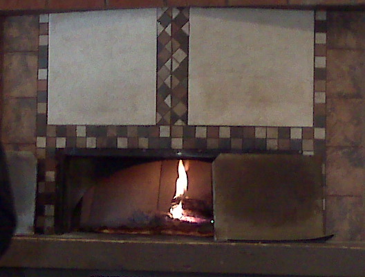 a fire inside a brick oven with multiple pieces of pizza on top