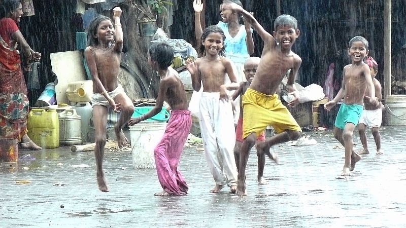 young children play in the rain outside of a shack