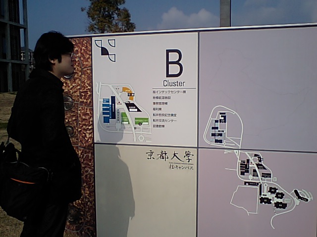 an asian male standing by a sign and looking in a direction