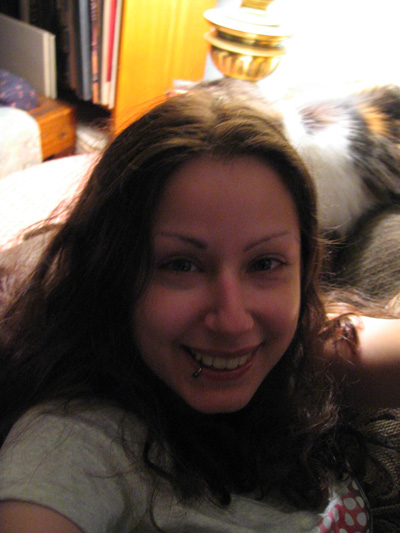 a woman is smiling on a bed with a cat behind her