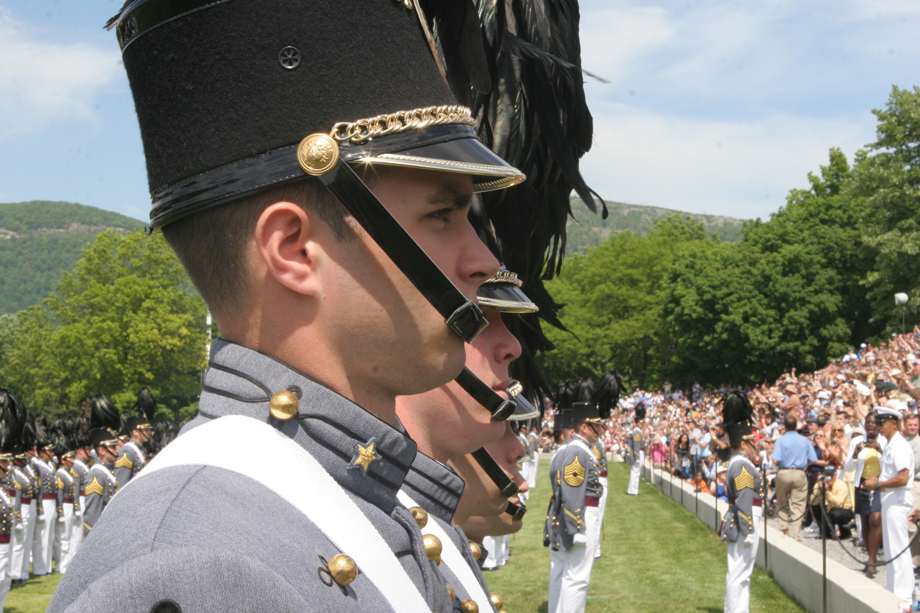 two men wearing dress uniforms stand in front of a crowd of people