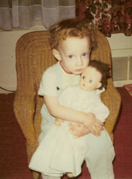 a little boy sitting in a chair holding a baby doll