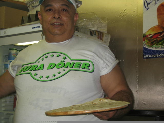 a man in the kitchen holds a large loaf of bread