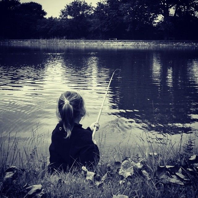a little girl sitting in the grass on the shore of a lake