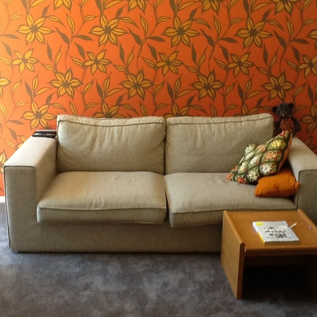 an orange floral wallpaper a gray sofa and a small table