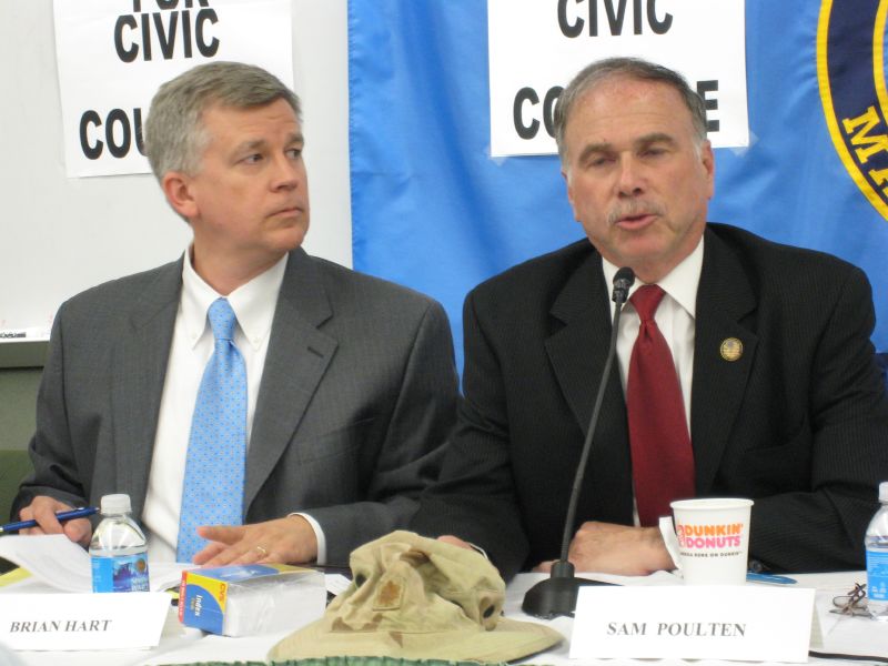 two people sitting at a table with signs behind them