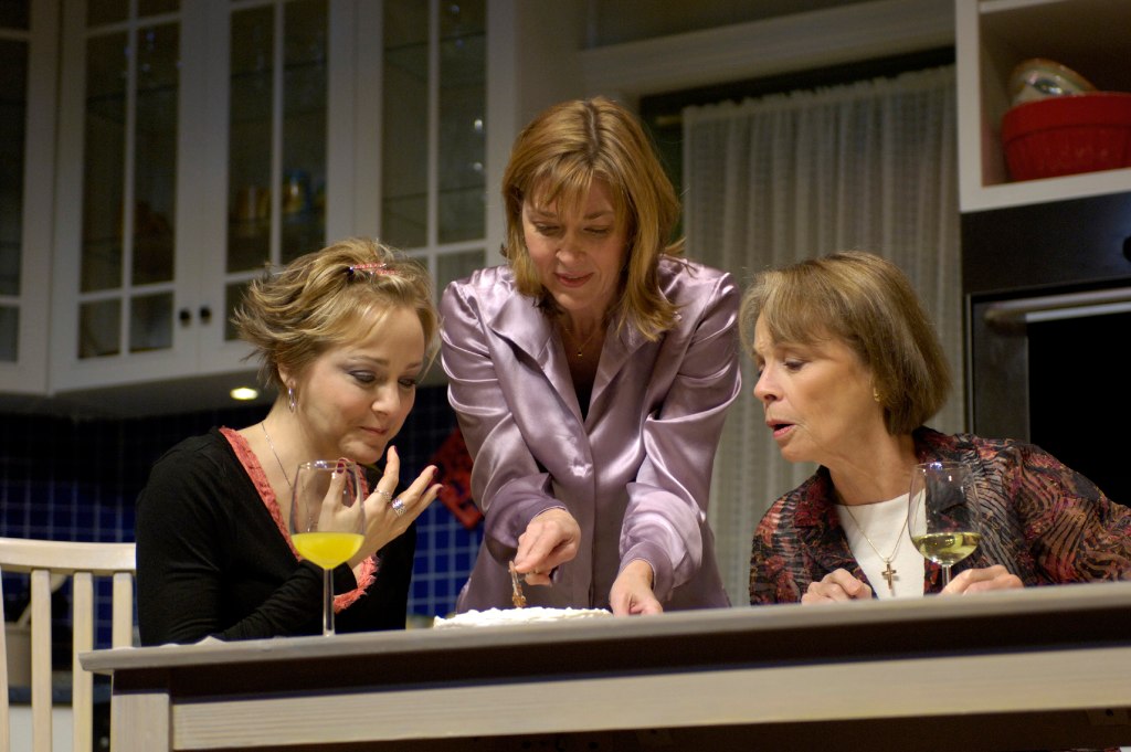 three women eating cake in a large kitchen