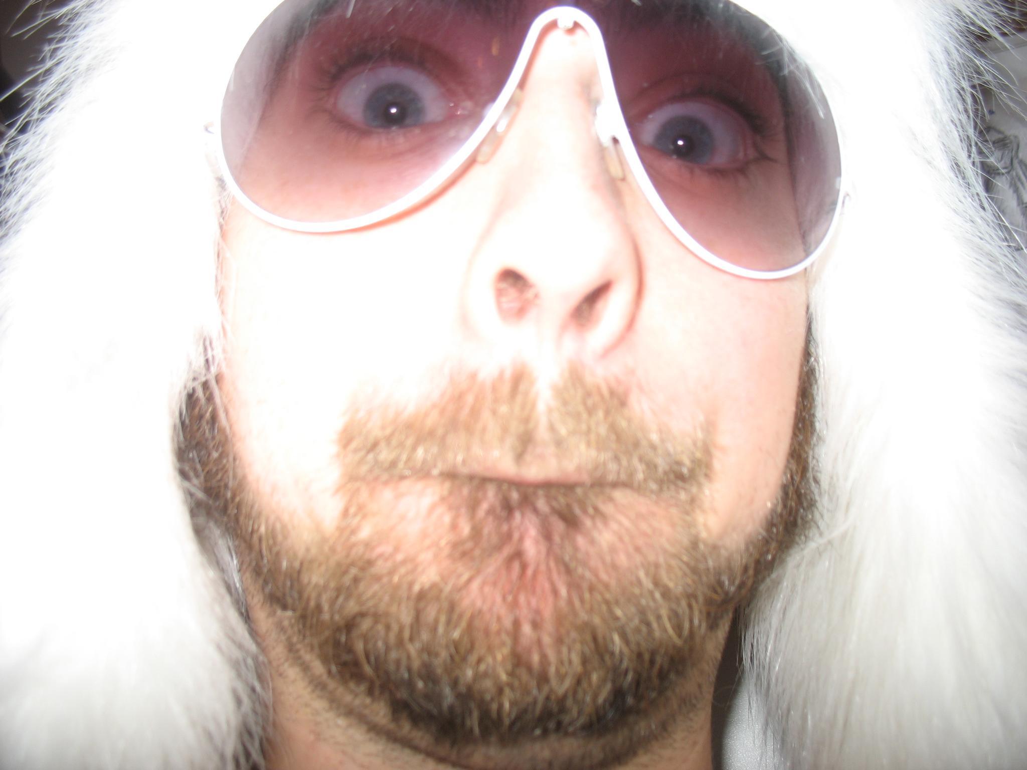 a man with sunglasses wearing a furry coat and looking at the camera