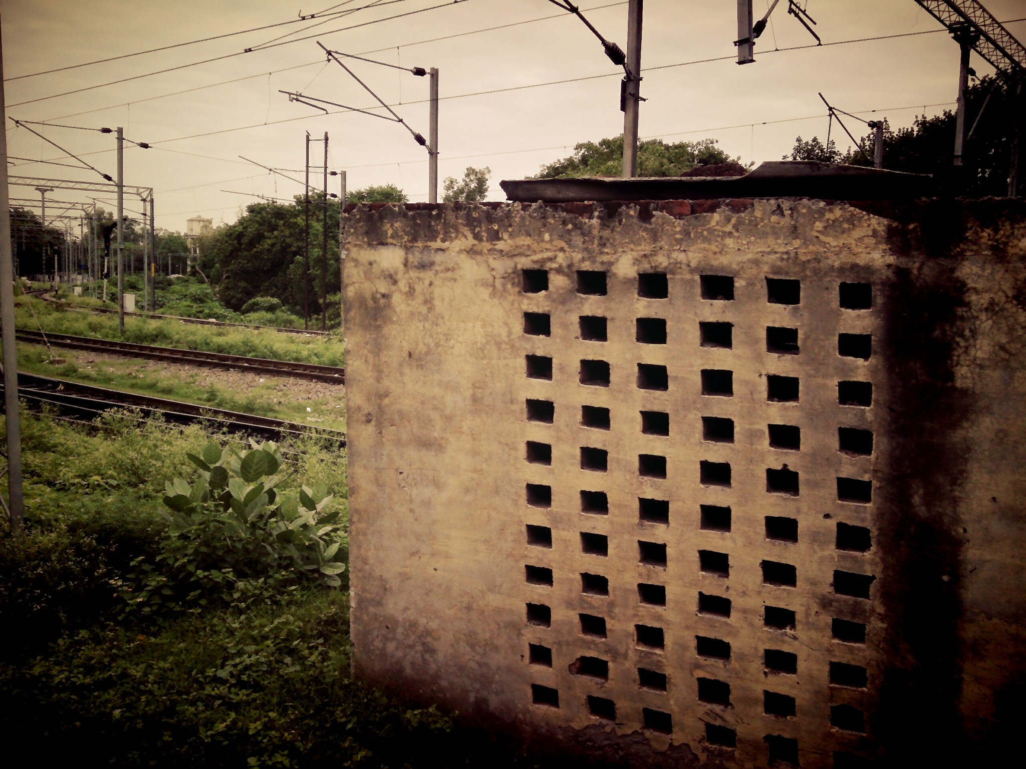 a rusty rusted cement wall near train tracks and electrical wires