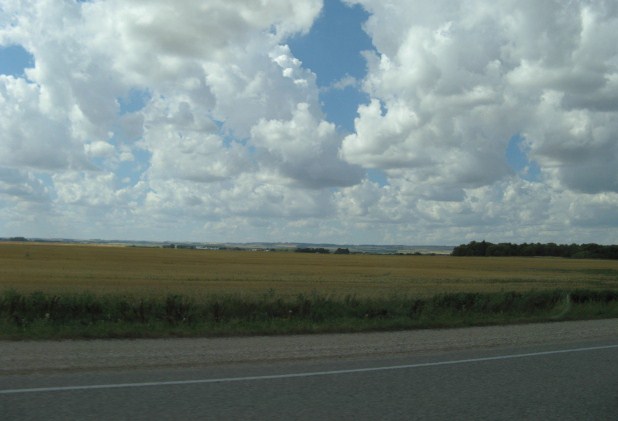 a road next to an empty field with clouds