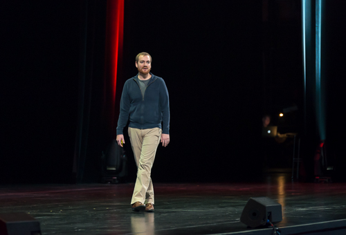 man on stage wearing sandals and a sweater