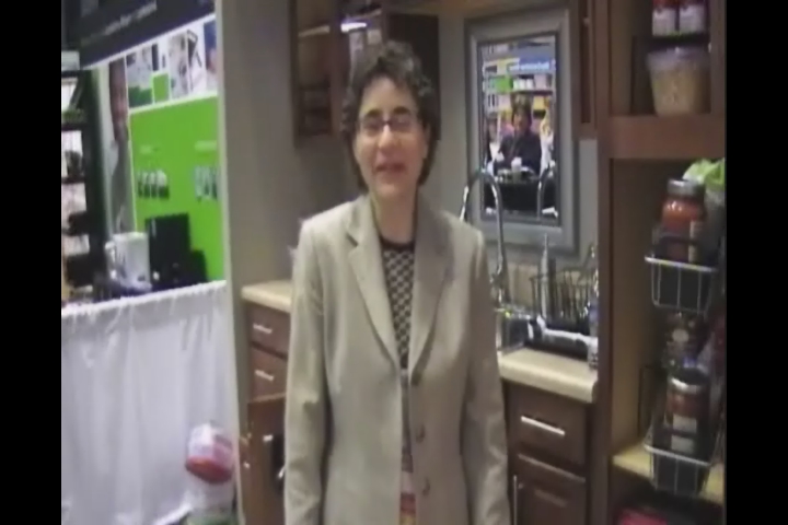 a woman in suit and glasses stands next to a kitchen with cabinets
