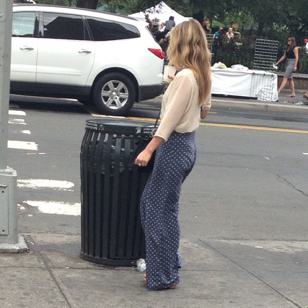 a woman standing on a street next to a garbage can