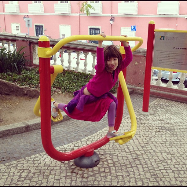 a little girl in purple is swinging on a red and yellow playground structure
