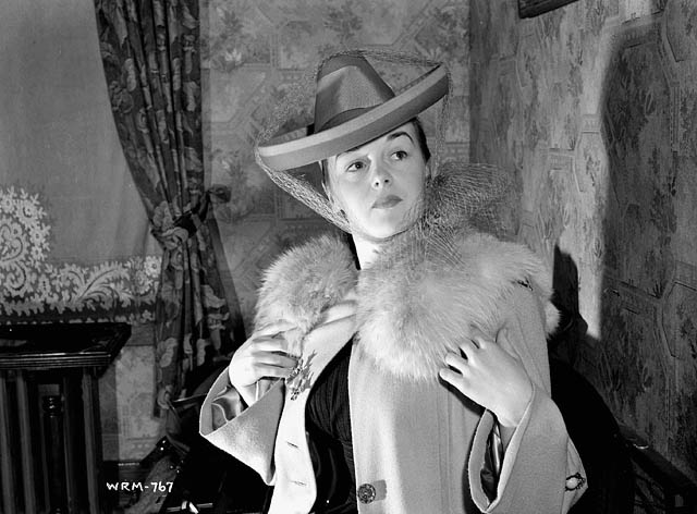 a woman wearing a large hat while standing next to a chair