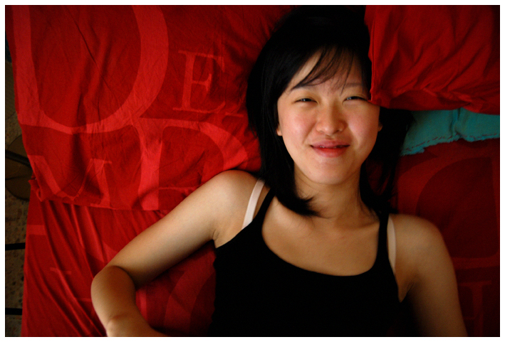 a woman laying on top of red sheets and covering the camera
