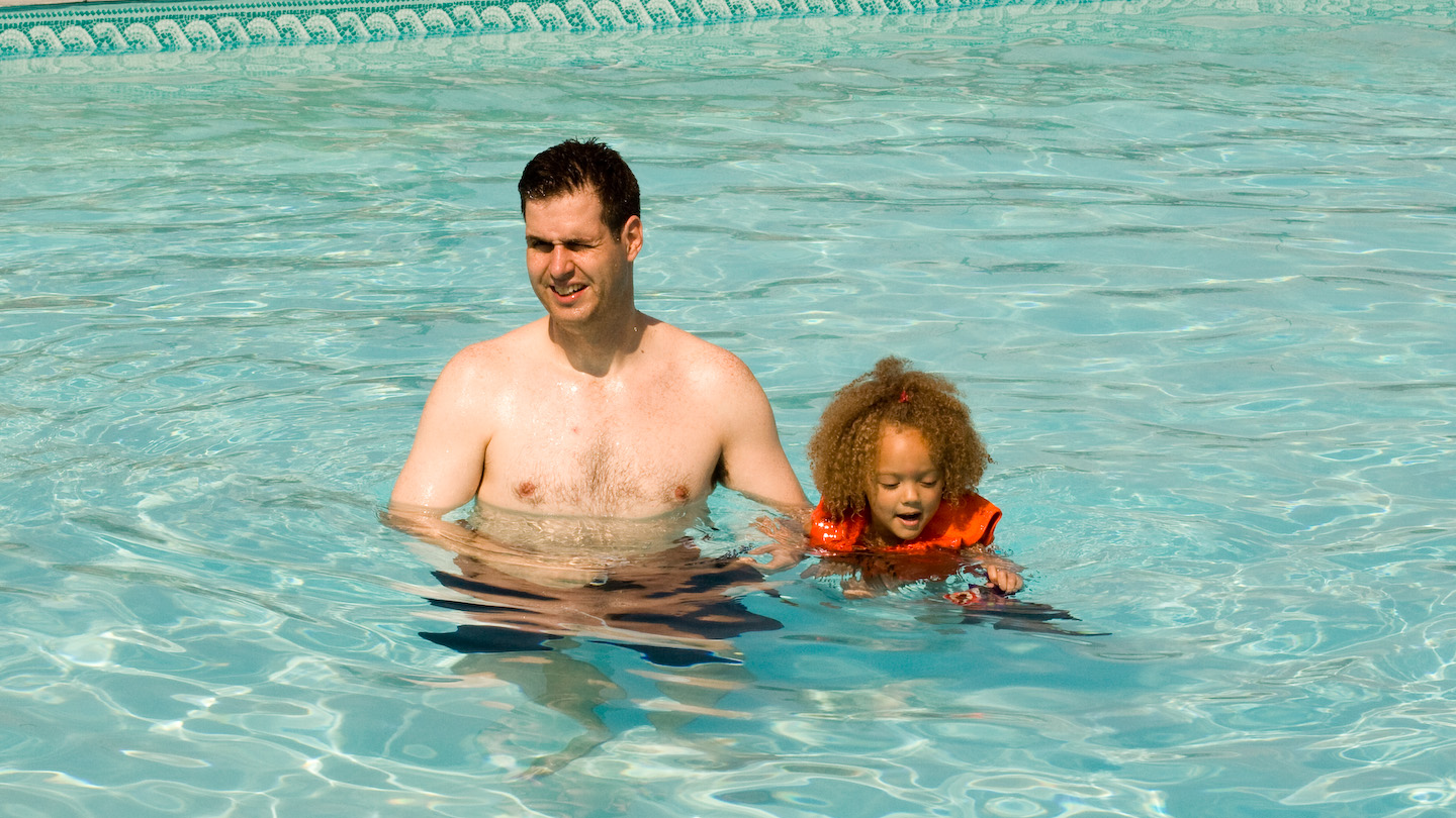 man and child swim in large pool wearing swimming trunks