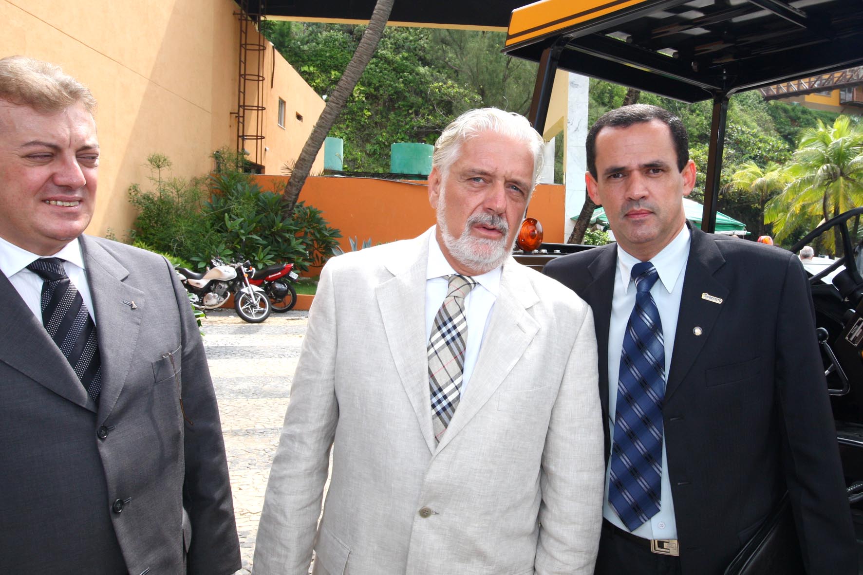 three men in suits standing near a golf cart