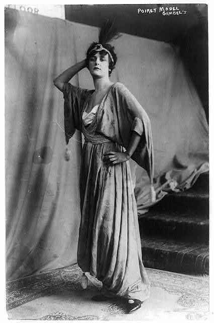 a woman in a long dress standing with her arms on her head