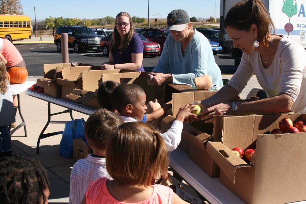 two woman handing apples to a group of young children