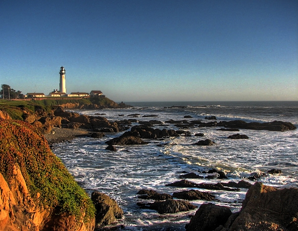 a lighthouse near the ocean with waves in the foreground