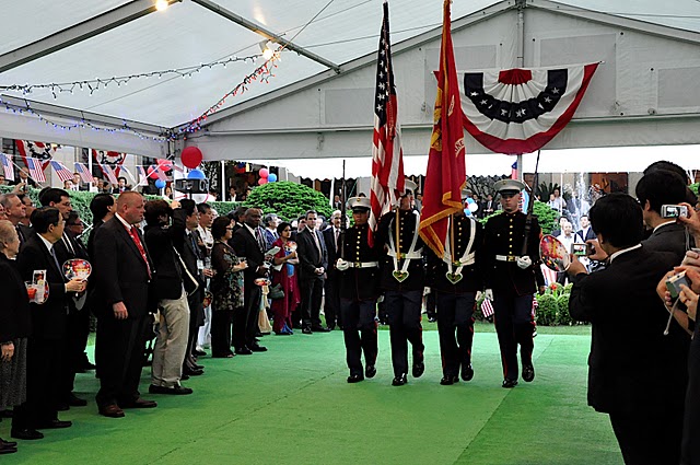 group of people in uniform are on green carpet near white tent with a flag