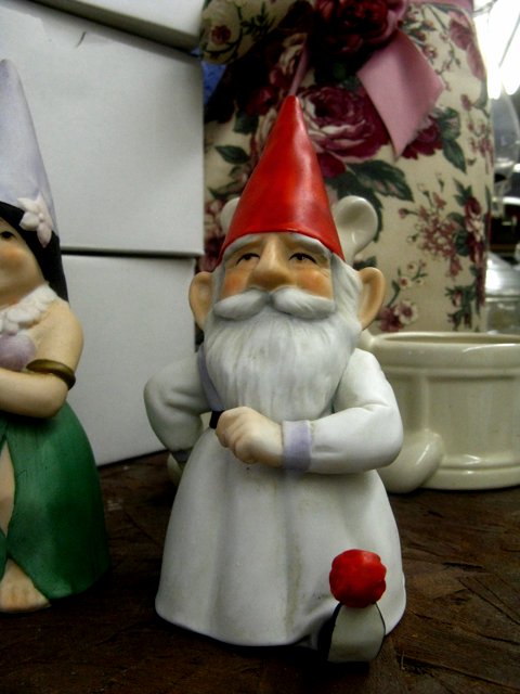 two gnomes sit beside one another and one is holding a rose