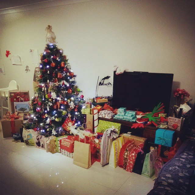 a large christmas tree in the corner next to a bed with presents on it
