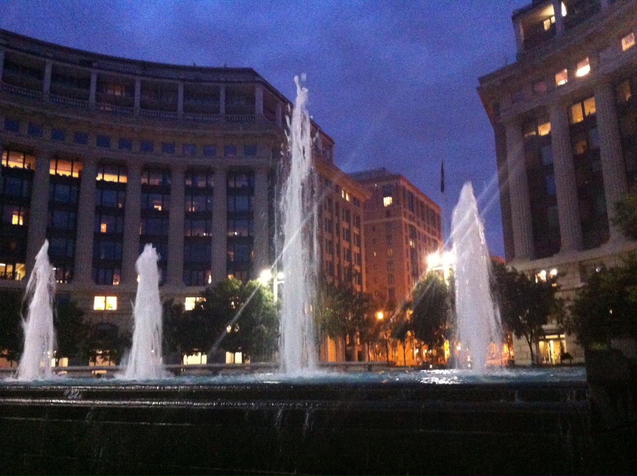 several fountain lights are seen at night in a city