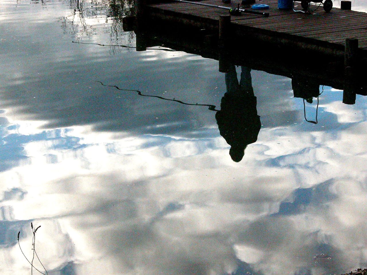 a dock and water reflecting the sky and clouds