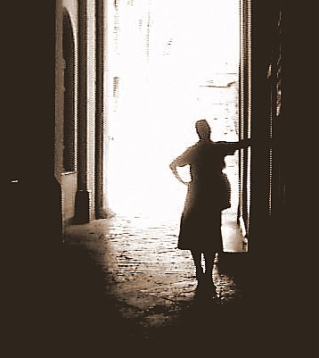 a woman holding her hand out to the light shining through an open doorway