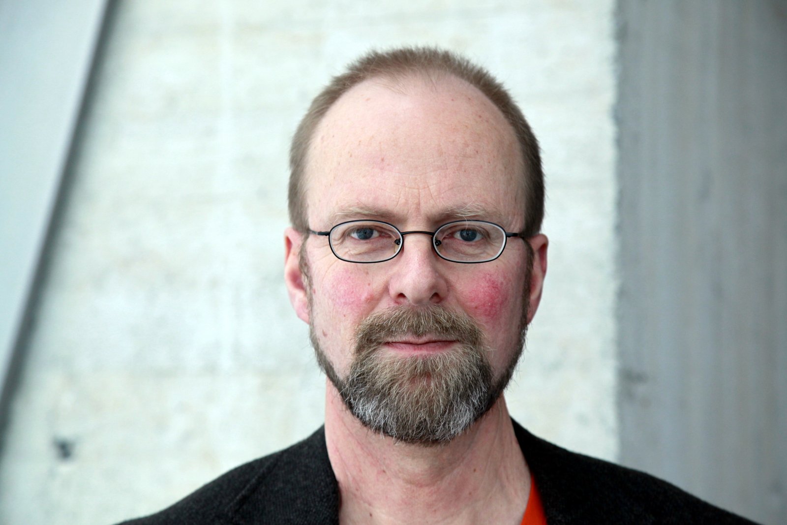 a man with glasses is smiling in front of a wall