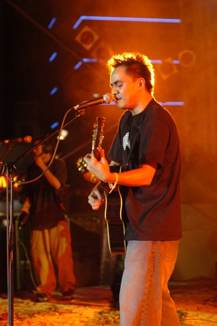a boy in a microphone plays guitar while another band member looks on
