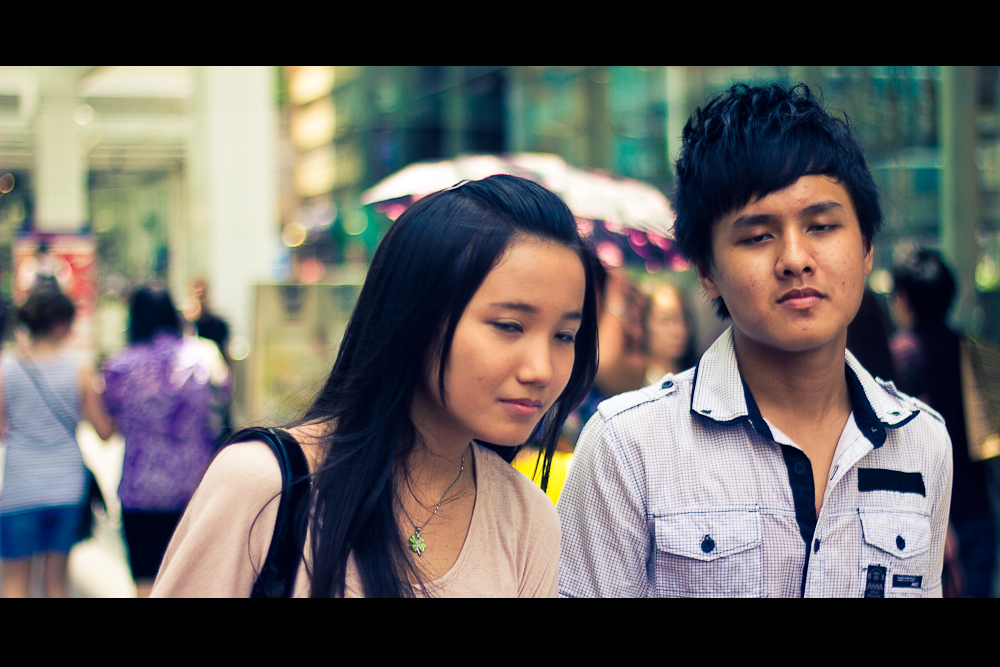 young couple staring at cell phone while standing on sidewalk