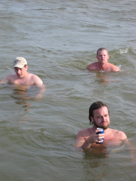 three men swimming in the ocean with a frisbee