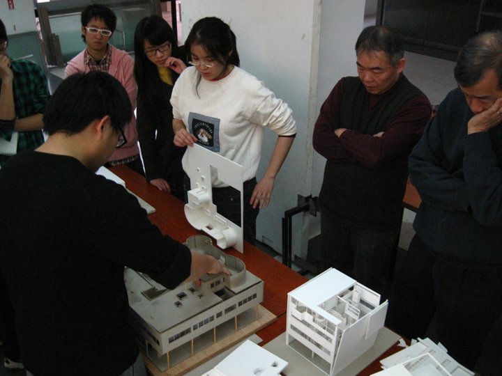 a group of people standing around a small model building