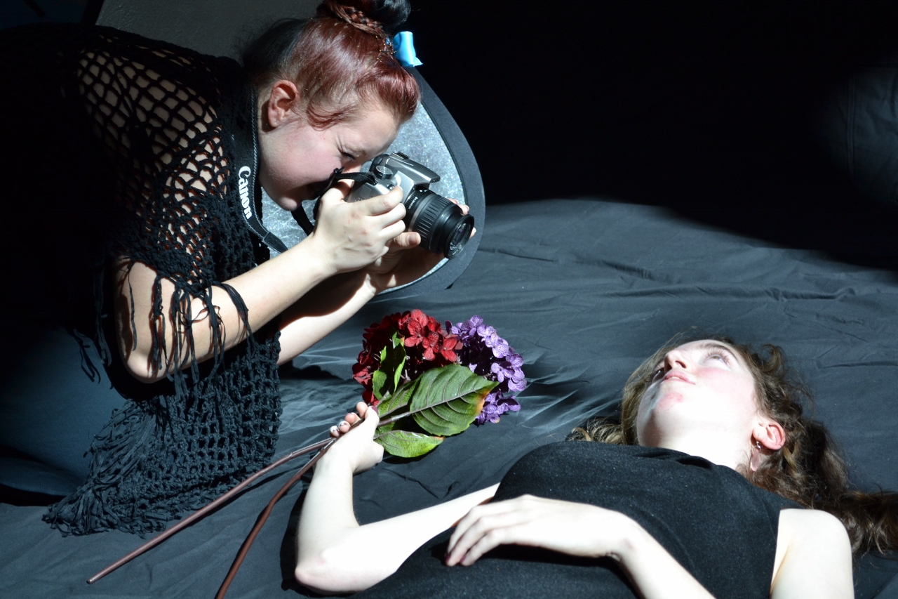 a lady on a bed getting makeup done by a woman lying down